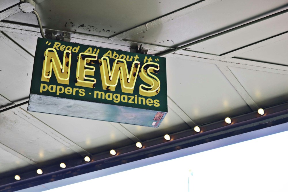 A neon sign for the news hanging above a street