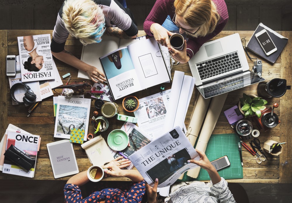 A table covered with different media and people working above it