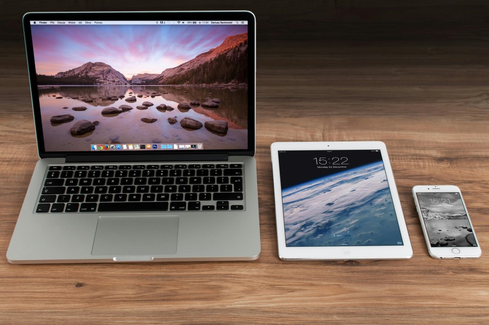 A laptop, tablet, and phone lined up on a wooden desk